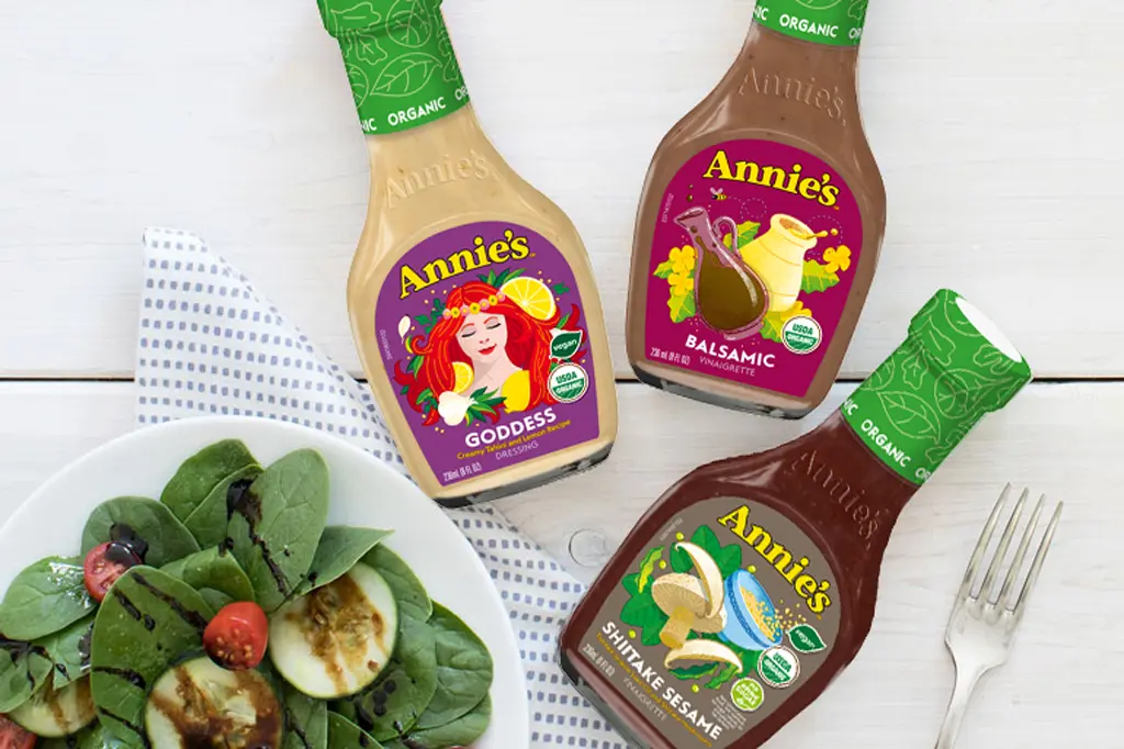 A single bottle of Annie's Organic Goddess Dressing, Annie's Organic Balsamic Vinaigrette and Annie's Organic Shiitake Sesame Vinaigrette next to a plate of spinach salad and a fork.