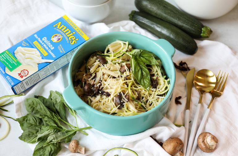 Gluten Free Quinoa Zucchini Mac in a bowl with ingredients scattered round it and Annie's Quinoa box next to it.