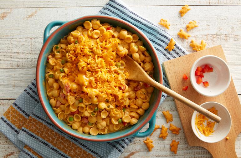 A crock pot filled with cheesy pasta with a wooden serving spoon in it
