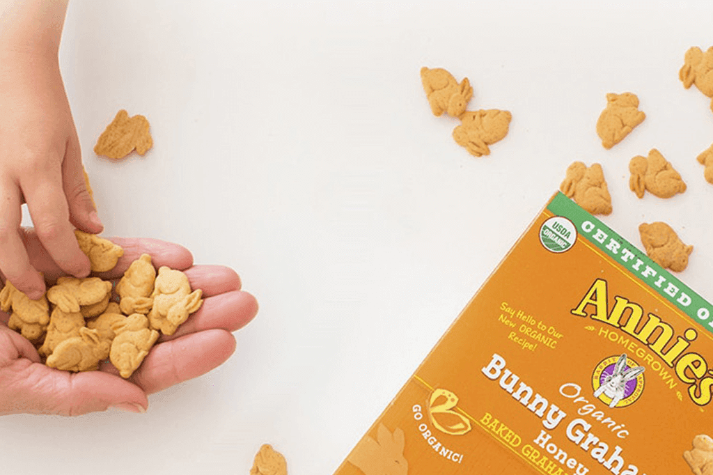 Child picking Annie's Bunny Grahams out of an adult's hand, with the package and scattered Bunny Grahams nearby.