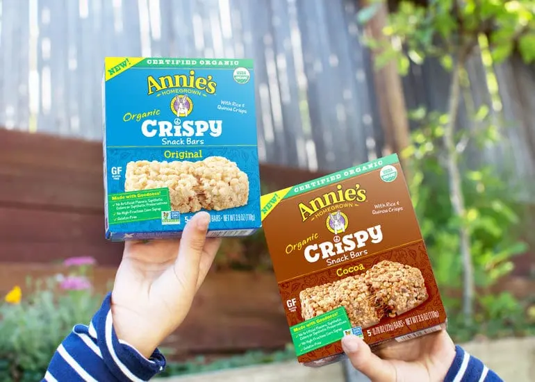 A child's hands hold up two boxes of Annie's Organic Crispy Snack Bars.