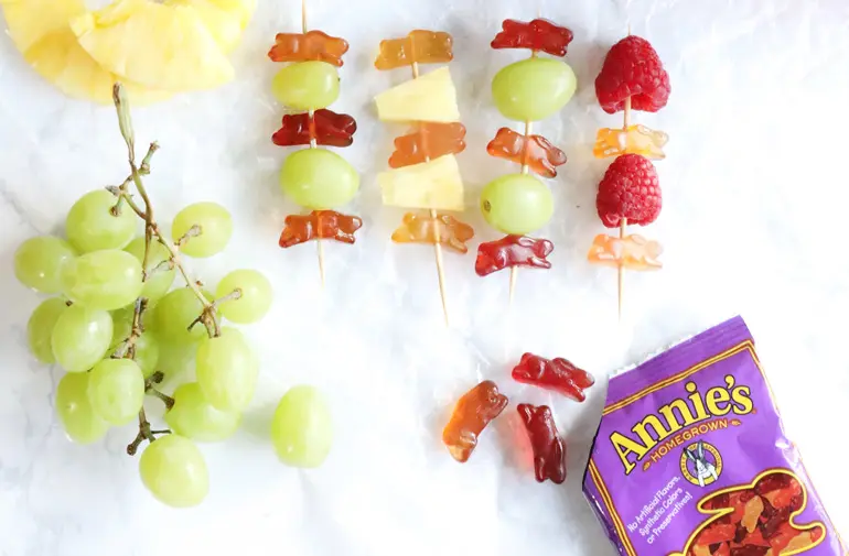 Fruit skewers with fruit snacks on them as well as fresh fruit there are grapes beside the skewers