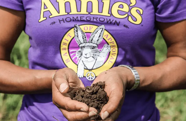 Woman in an Annie's t-shirt with her hands full of organic soil.