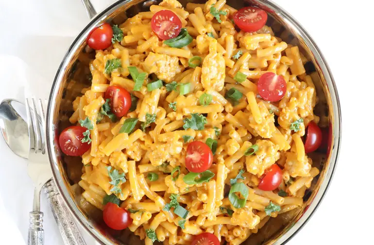A bowl of cheesy pasta with fresh cherry tomatoes and spring onions