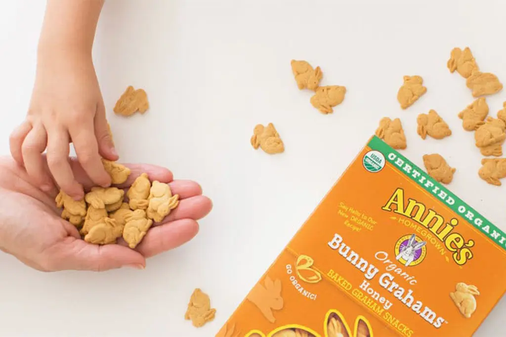 Child picking Annie's Organic Bunny Grahams out of an adult's hand, with the package and scattered Bunny Grahams nearby.