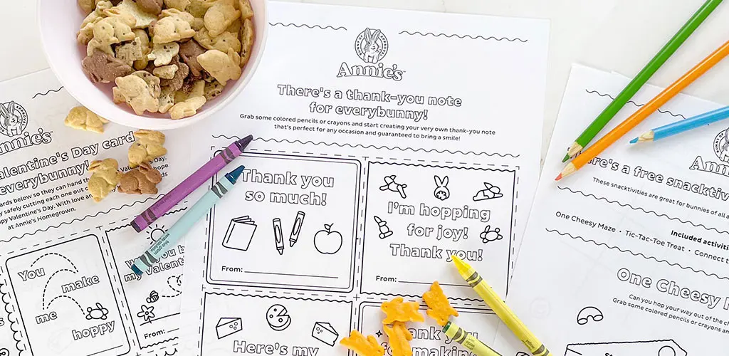 Three different Annie's activity sheets laying out with single Cheddar Bunnies sprinkled around, Bunny Grahams in a bowl, and a few colored pencils and crayons.