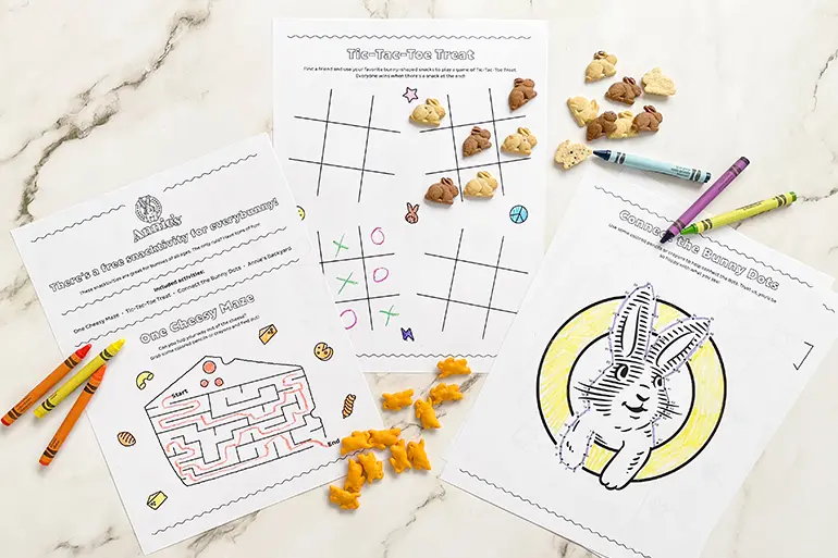 Three different Annie's Activity Sheets arranged on a marble slab with single Bunny Grahams and Cheddar Bunnies, as well as some crayons.