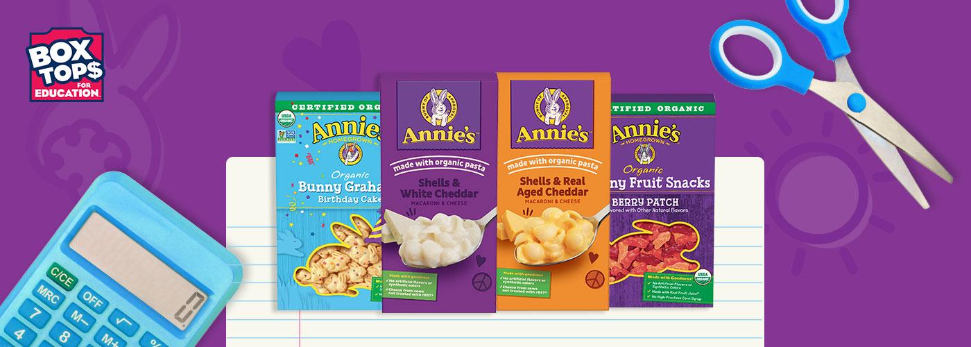 Collage image of four packages of different Annie's products on a purple background with a Box Tops For Education logo, notebook paper, a calculator and a scissors.