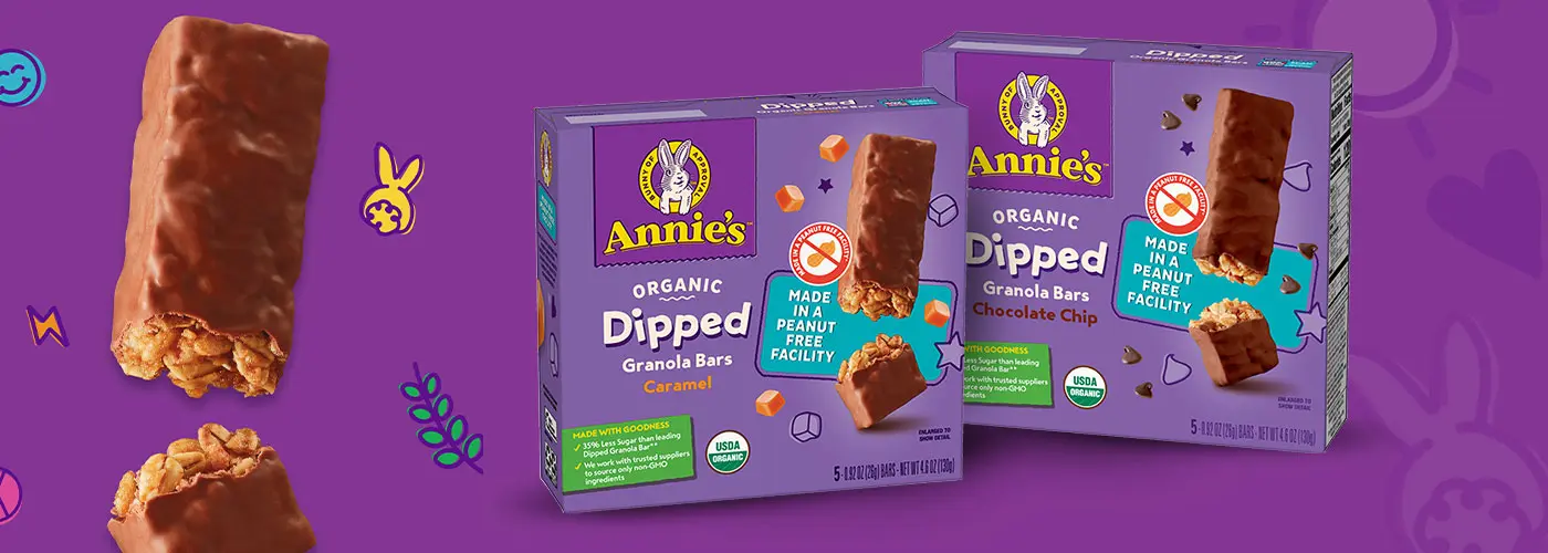 A single dipped granola bar next to single boxes of Annie's Organic Dipped Granola Bars Caramel and Annie's Organic Dipped Granola Bars Chocolate Chip. Each package has a "Made in a peanut free facility" statement on the front.