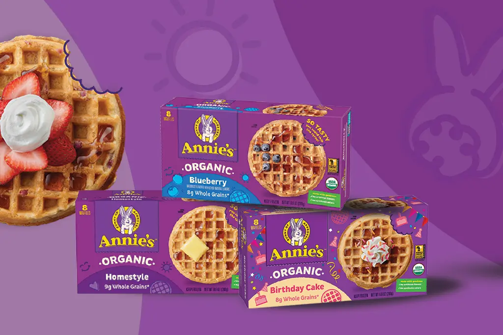A waffle photo with strawberries and whipped cream next to a single box of Annie's Organic Blueberry Waffles, Annie's Organic Homestyle Waffles and Annie's Organic Birthday Cake Waffles on a purple background.