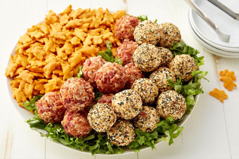 A platter of two different kinds of stacked Mini Cheeseballs on a bed of lettuce on half the plate and Annie's Organic Cheddar Bunnies Baked Crackers on the other half.