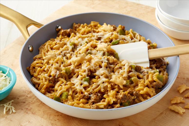 Philly Cheesesteak Mac & Cheese in a skillet with a spatula and sitting on a counter top.