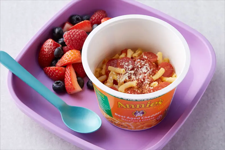 Pizza Mac & Cheese Cup recipe in an Annie's Real Aged Cheddar Microwaveable Macaroni & Cheese on a purple plate with strawberries and blueberries.