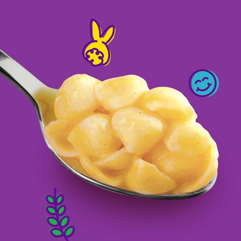 A close up image of a silver spoonful of Annie's Mac & Cheese with a purple background.