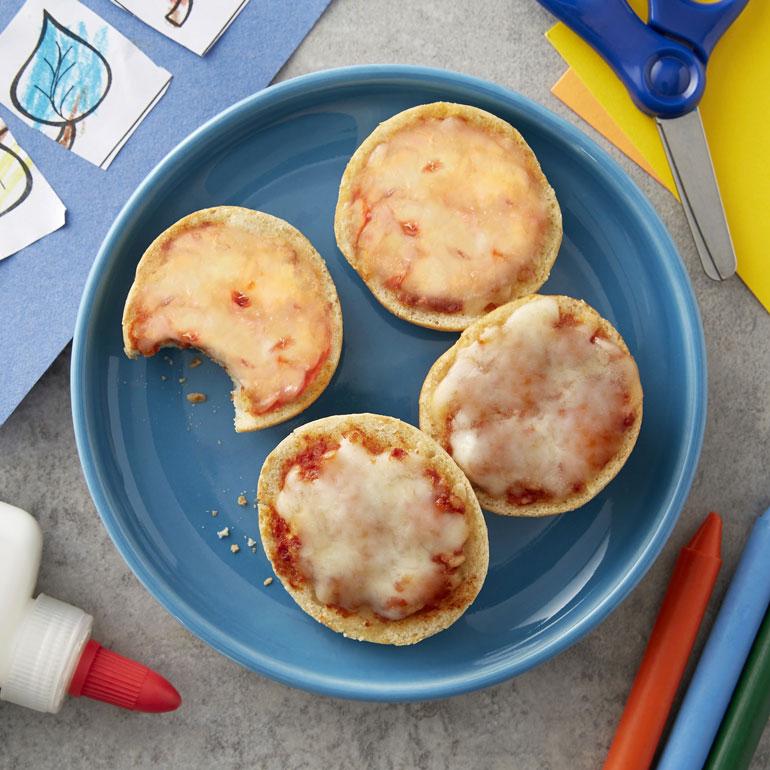 Four Annie's Mini Pizza Bagels on a blue plate with some school supplies showing.