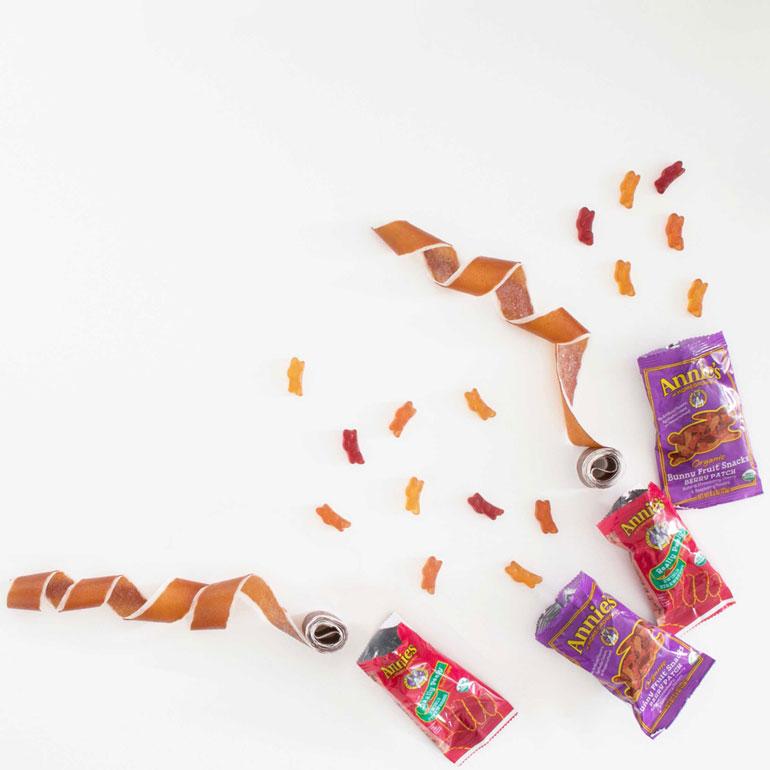 Four opened snack packages partially showing Annie's Fruit Tape and some Annie's Fruit Snacks sprinkled around.