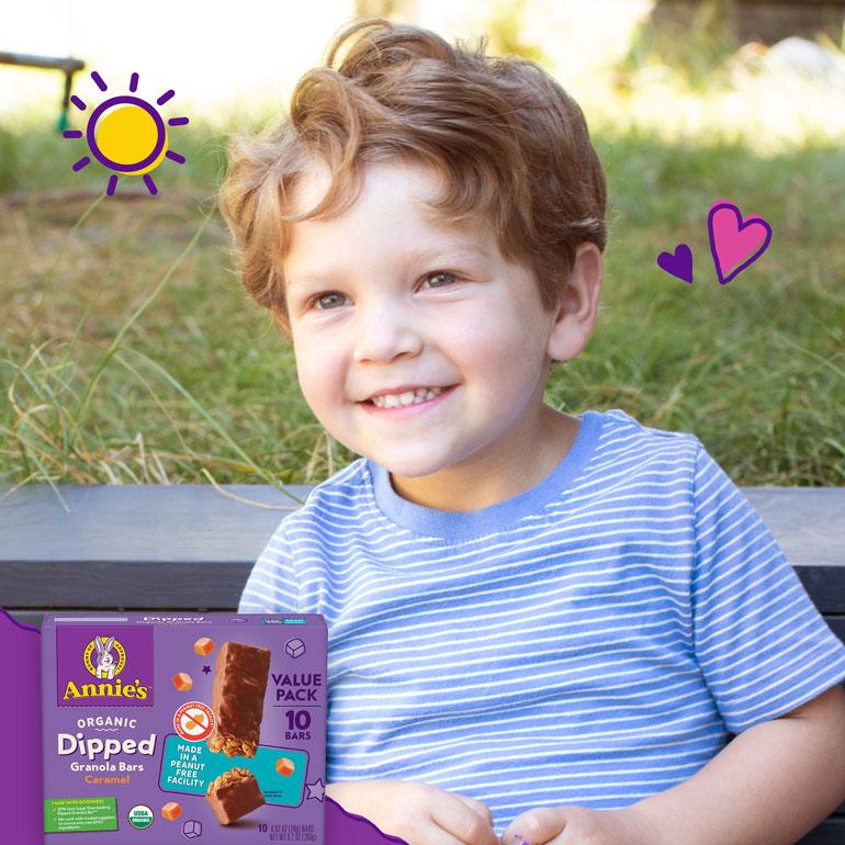 Small child smiling with Annie's Organic Dipped Granola Bar Caramel front of package.