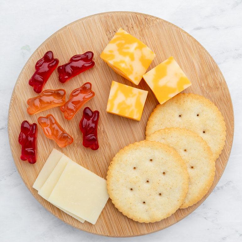 Small wooden plate with Annie's Fruit Snacks, round crackers, white and marbled cheese slices.