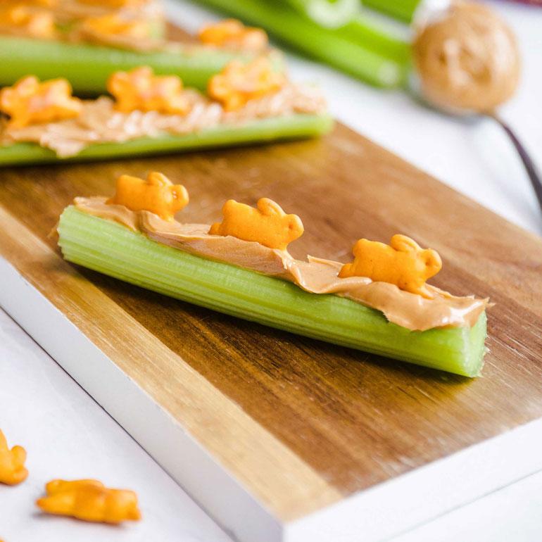 Snack-sized pieces of celery with peanut butter and Annie's Cheddar Bunnies on a table.