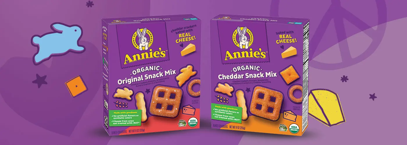 Single boxes of Annie's Organic Original Snack Mix and Annie's Organic Cheddar Snack Mix on a purple background.