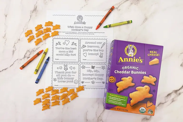 Annie's "Wish mom a Hoppy Mother's Day" coloring activity lying with a box of Annie's Cheddar Bunnies, single fruit snacks and crayons.