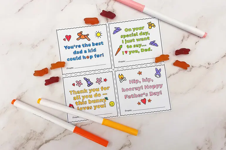 Annie's "Father's Day" themed colorings with sayings like, "You're the best dad a kid could hop for," and three markers and single fruit snacks laying out.