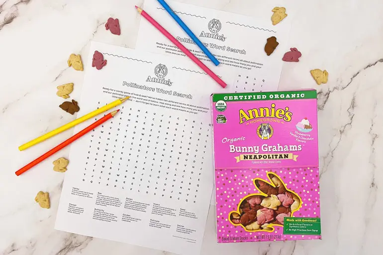 "Annie's Pollinator word search" lying on a marble table with Annie's Neapolitan Bunny Crackers and colored pencils displayed.