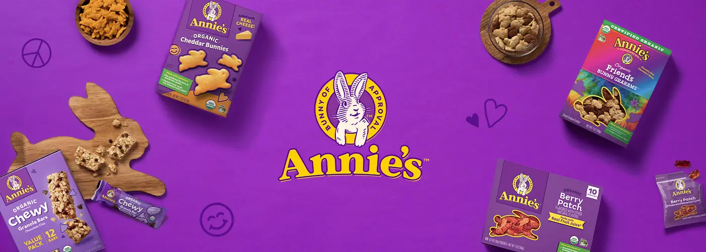 Annie's logo on a purple background with the front of snack packages and bowls of Cheddar Bunnies and Bunny Grahams and a single chewy granola bar.
