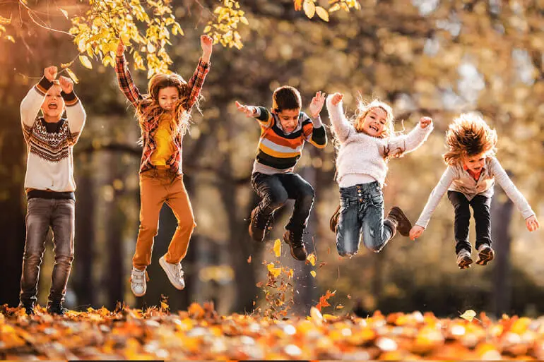 A group of kids jumping in the air with fall leaves in the foreground and background.