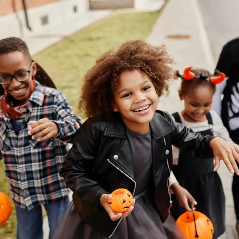 A group of kids dressed up in Halloween costumes holding mini pumpkins.