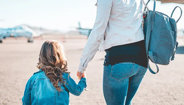 A close up photo of a parent holding a child's hand outside at an airport.