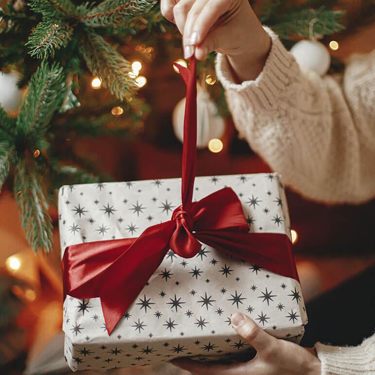 A person holding a gift wrapped in a red ribbon