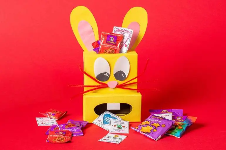 A yellow bunny box filled with Annie's snacks & activity cut outs in front on a red background