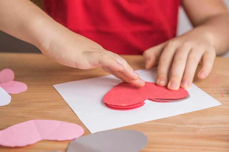 A child crafting a heart out of red paper