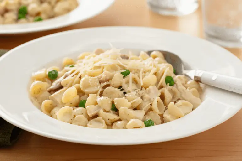 Creamy chicken pasta with peas and parmesan in a white bowl with a white spoon.