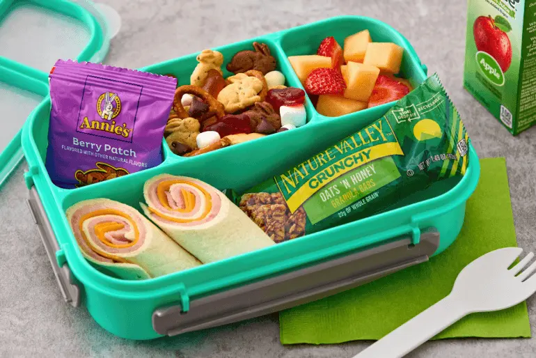 Kid's lunchbox with ham and cheese roll-ups, Annie's Berry Patch snacks, Nature Valley granola bar, fruit, and juice box.